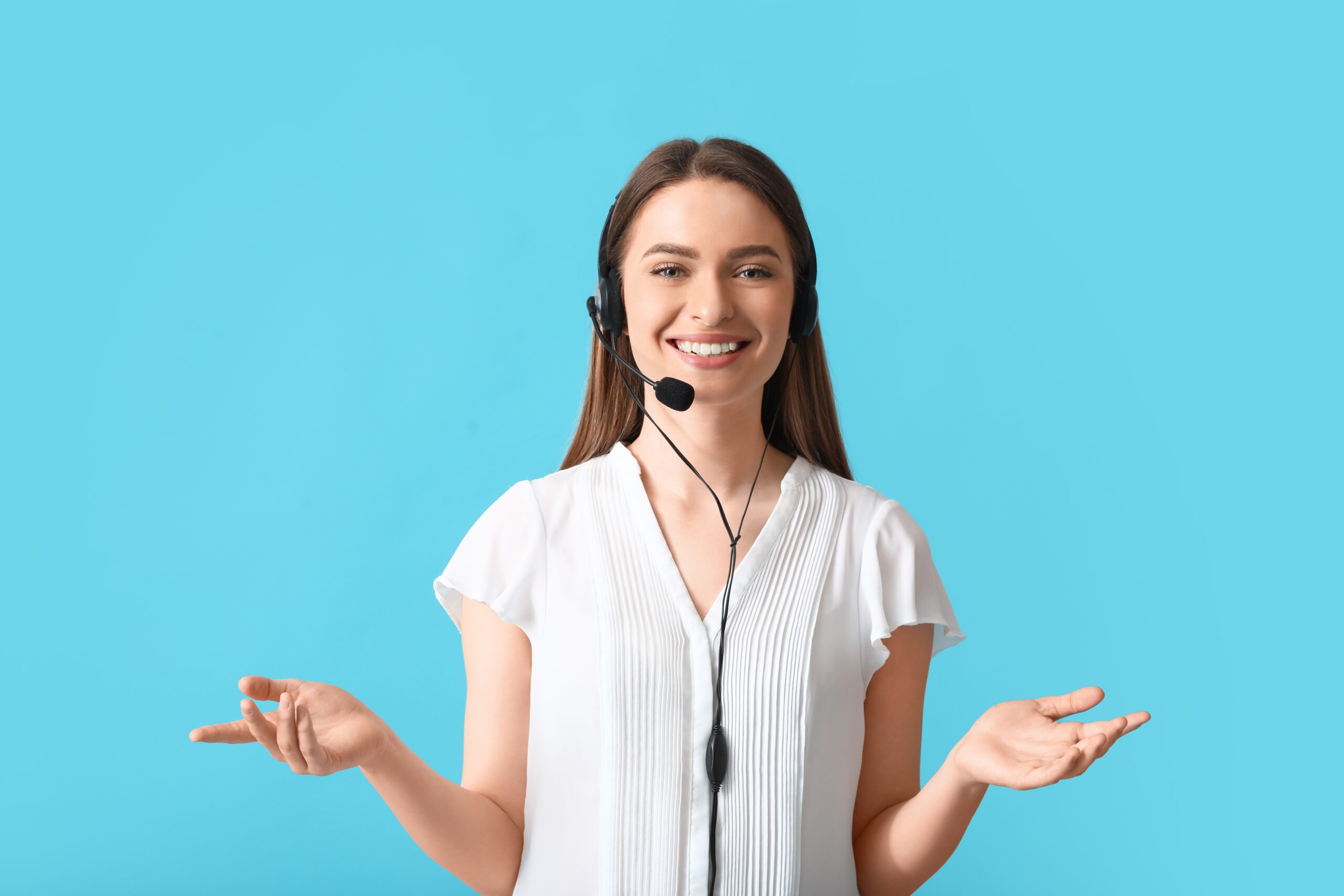 Smiling woman in a white blouse wearing a headset, gesturing with both hands against a bright teal background, indicating readiness for communication.
